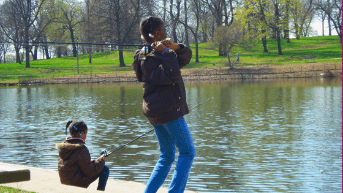 Two young girls fishing off a dock on a small lake.