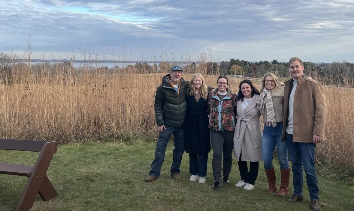Group of employees standing with arms around each other in a field.